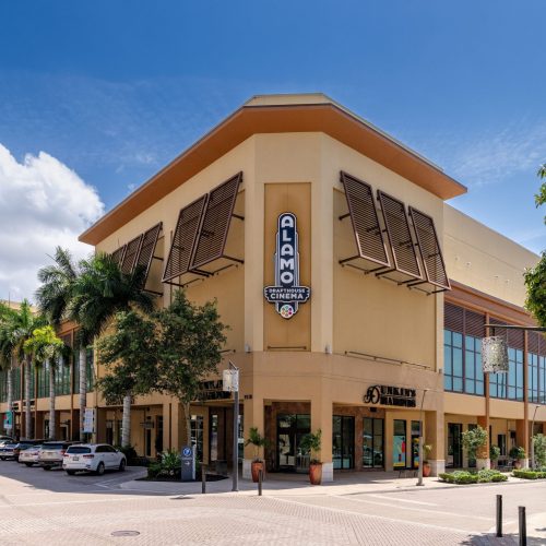 The front view of Alamo Drafthouse Cinema with nearby shops and parking spaces in the foreground.